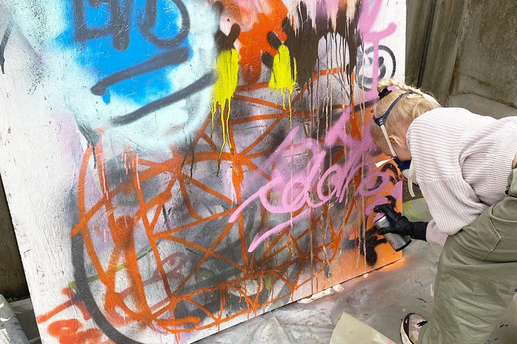 Billede af pige med maske, der laver graffiti paa laerred